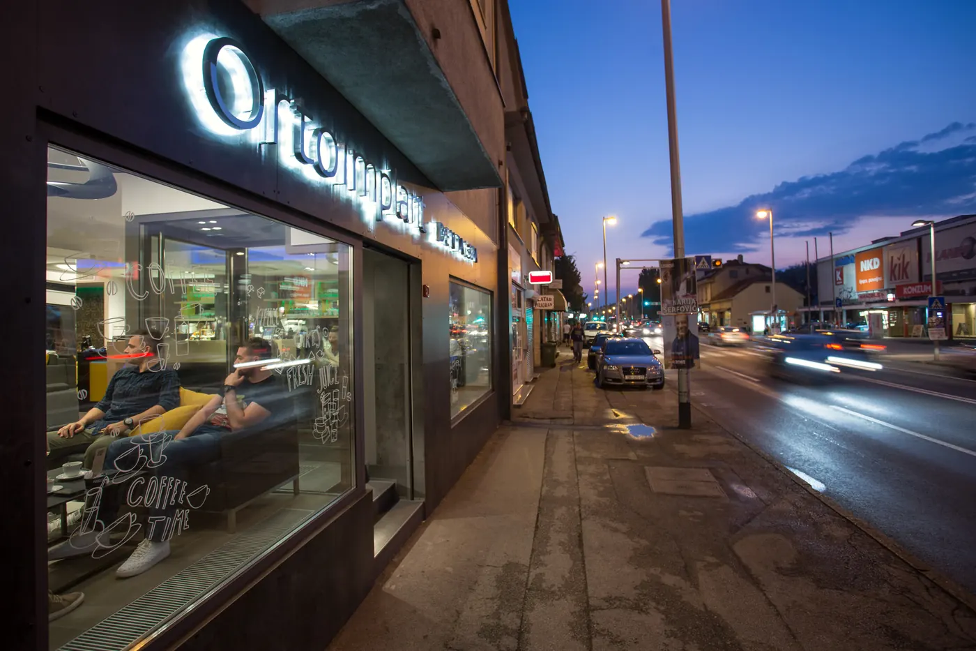 Pročelje zgrade u Ilici 283 u sumrak, s natpisom Ortoimplant DENTAL SPA i osvijetljenim izlozima kafića